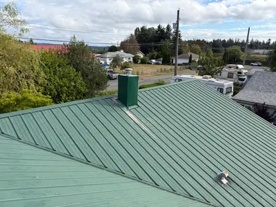 Wide view of a green metal roof, matching chimney encasement and intersecting roof slopes in Campbell River.