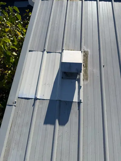 Box-shaped fan vent with a rectangular flashing section on a light-grey metal roof in Campbell River.