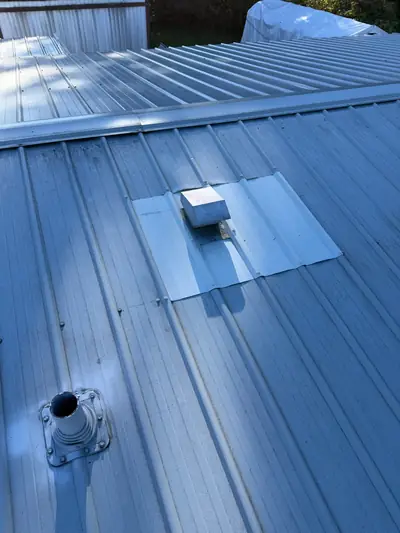 Fan vent surrounded by a light-grey flashing section on a Campbell River metal roof, with a separate pipe nearby.