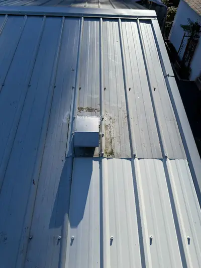 Fan vent and flashing below the ridge of a ribbed metal roof, photographed during a Campbell River repair.