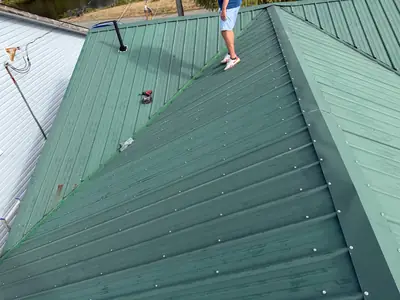Screw fasteners across green metal roof panels and hip flashing, with tools visible during work in Campbell River.
