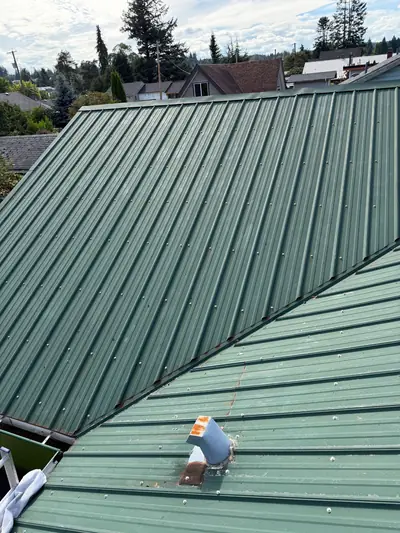 Connected green metal roof slopes with rows of exposed screw fasteners on a Campbell River property.