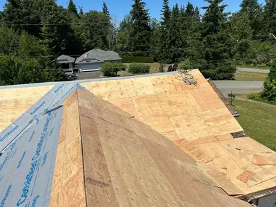 Plywood sheets over intersecting roof slopes, with underlayment along one slope and tools on the deck.