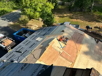 Roof deck being re-sheeted with plywood, with underlayment on one slope and cedar removal still underway at the far edge.