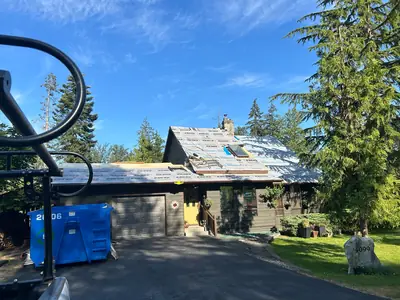 House and garage with exposed roof underlayment around a skylight and chimney, with plywood and site equipment still visible.