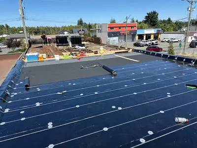 Low-slope roof under construction with membrane layers, exposed decking and materials staged across the roof.