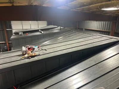 Several dark metal roof sections with raised seams and flashings inside a workshop.