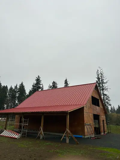 Red metal roofing over a steep upper roof and lower porch roof on an unfinished timber building.