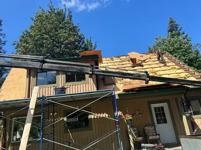 Roof work exposing framing and insulation, with new sheathing, scaffolding and a material conveyor.