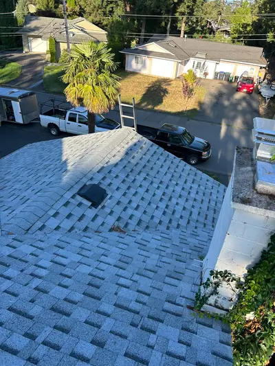 Light grey shingles along a hip roof with a black box vent and a chimney in the foreground.