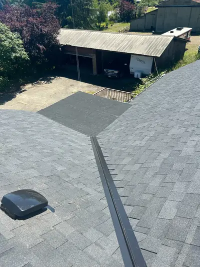 Close view of a metal valley between two grey shingle slopes with a black box vent nearby.