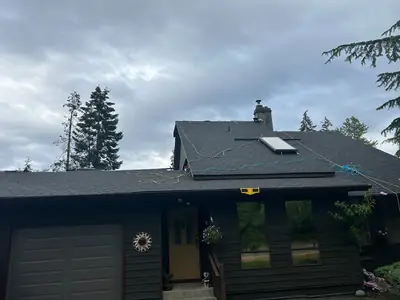 Dark grey shingle roof with a skylight, chimney and temporary work lines on the roof.