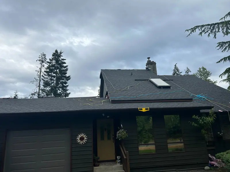 Dark grey shingle roof with a skylight, chimney and temporary work lines on the roof.