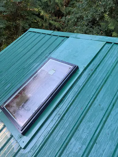 Installed rectangular skylight with green metal flashing extending up the slope of an existing green metal roof.