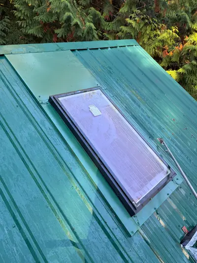 Closer angled view of an installed skylight, its side and lower flashing, and the green metal roof around it.